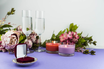 Obraz na płótnie Canvas Marriage proposal and love concept for Valentine`s day, box with wedding or engagement ring with brilliant. Glass of champagne, romantic dinner, peony flowers and candles on trendy purple background