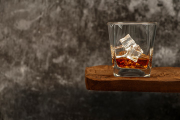 Whiskey with ice or brandy in a glass on a rustic table and gray background. Whiskey with ice in a glass. Whiskey or cognac in a glass. Selective focus.