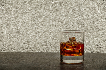 Whiskey with ice or brandy in a glass on a rustic table and gray background. Whiskey with ice in a glass. Whiskey or cognac in a glass. Selective focus.