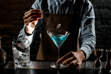 Male bartender deacorating a blue alcoholic cocktail in a martini glass with a spikelet