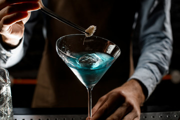 Professional male bartender deacorating a blue alcoholic cocktail in a martini glass with a spikelet