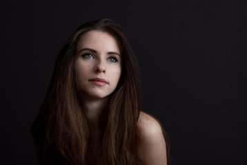 Fototapeta premium Sad girl with naked shoulders against a dark background. Dramatic image.