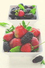 Fresh ripe mulberries and strawberries with mint in bowl on white background, copy space