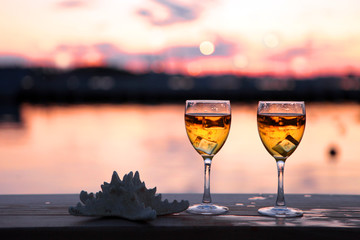 Two Glasses of white wine and drops of ice cubes against red sunset in yachting port. Beautiful summer evening sea view. Vacation for couple. Romantic evening