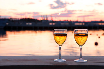 Two Glasses of white wine and drops of ice cubes against red sunset in yachting port. Beautiful summer evening sea view. Vacation for couple. Romantic evening
