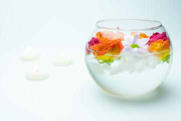 Selective focus of colorful flowers in vase with ice and burning candles at background on white surface 