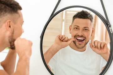 Handsome man flossing teeth at home