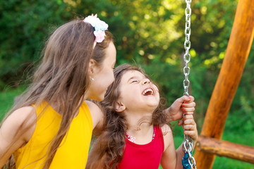 Two happy beautiful girls sitting on swing and smiling at warm  summer day