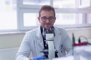 Naklejka na ściany i meble Young male scientist looking through a microscope in a laboratory doing research, microbiological analysis, medicine.