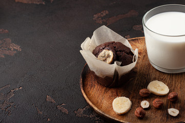 Homemade chocolate muffin in pastry with cup of milk on wooden plate. Close-up.
