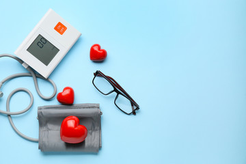 Sphygmomanometer, glasses and red hearts on color background