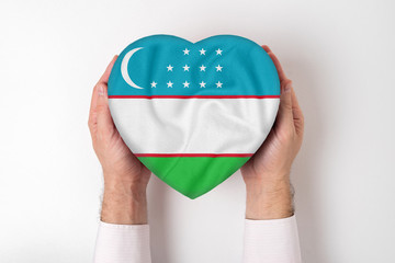 Flag of Uzbekistan on a heart shaped box in a male hands. White background