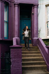 Young woman leaving her house and using her smart mobile with colorful houses on Portobello Street in the Notting Hill neighborhood