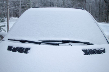 Snow covered car in the winter forest. The windshield is covered with snow.