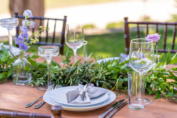 Beautifully decorated wooden table in a summer open-air cafe. Green branch and fresh flowers table decoration