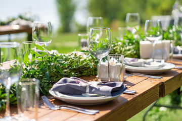 Beautifully decorated wooden table in a summer open-air cafe. Green branch and fresh flowers table decoration