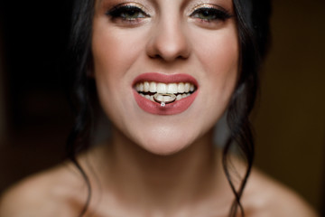 Close up portrait of gorgeous beauty young bride showing her wedding ring holding in teeth and smiling. Beautiful bride with diamond ring