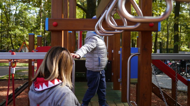 Chłopiec bawi sie na placu zabaw. Skacze na trampolinie i wspina się .