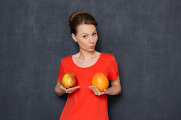 Portrait of impressed girl holding fruits in hands over chest