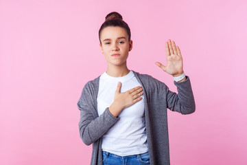 I swear. Portrait of serious honest teen girl with bun hairstyle in casual clothes holding hand on...