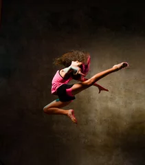 Gordijnen Streetdance meisje danser springen dansen in neon licht doen gymnastische oefeningen springen in studio op donkere muur © Dmitry Lobanov