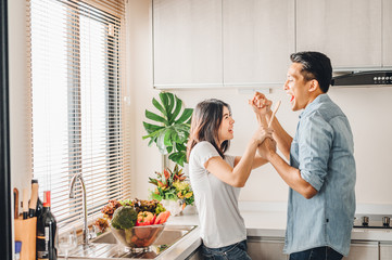 Asian couple in love is singing and dancing together in kitchen