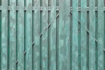 A fragment of a painted wooden gate. The structure of the boards and battens. Turquoise surround background.