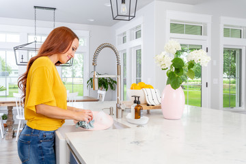 A woman washing dishes in a modern farmhouse kitchen. - Powered by Adobe