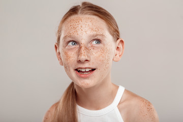 Inclusive Beauty. Girl with freckles and ponytail standing isolated on grey looking aside excited close-up