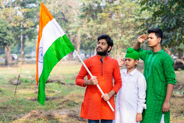 Three kids and young boys of different age and different religion hearing tricolor dress and holding Indian National flag. Indian kids celebrating Republic or Independence day of India. 