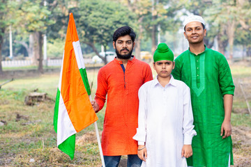 Three kids and young boys of different age and different religion hearing tricolor dress and holding Indian National flag. Indian kids celebrating Republic or Independence day of India. 