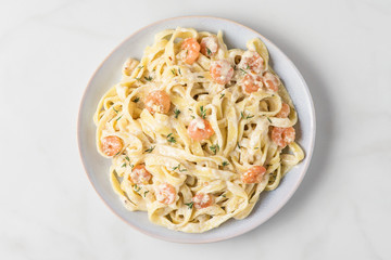 Italian pasta fettuccine or tagliatelle in a creamy sauce with shrimps in a plate on white marble table