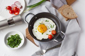 Fried egg with cherry tomato and green onion in frying pan, slices of bread. Tasty breakfast. Top view
