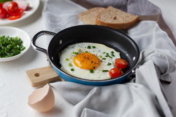 Fried egg with cherry tomato and green onion in frying pan, slices of bread. Tasty breakfast