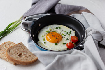 Fried egg with cherry tomato and green onion in frying pan, slices of bread. Tasty breakfast
