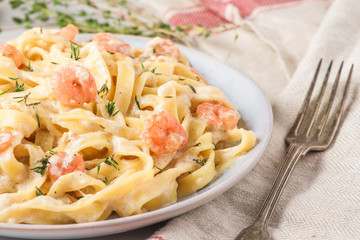 Italian pasta fettuccine or tagliatelle with shrimps in a creamy sauce with parmesan cheese and thyme in a plate
