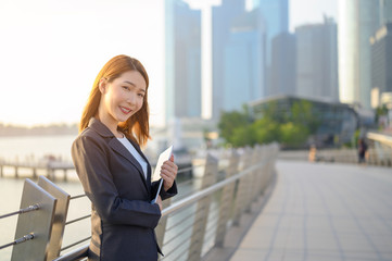 Young Asian business woman with Digital Tablet standing outdoors in modern city financial district. Business and  Technology concept