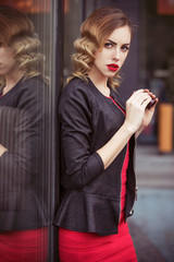 Beautiful brunette sexy spy agent (killer or police) woman in leather jacket and red luxury dress with a binocular in her hand stalking someone, to catch him in european city