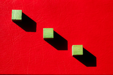 3 cubos de madera verde sobre fondo rojo y su sombra proyectada en diagonal