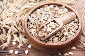 Oatmeal in wooden spoon on oat ears plants background, selective focus, toned