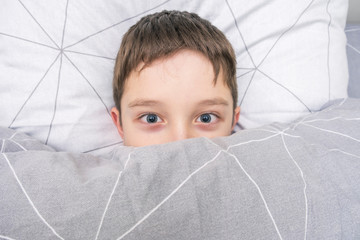 Top view of a scared boy in bed covering his face with blanket