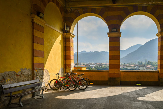 The arcade of the Civic Theatre of Dronero with a wooden bench, parked bicycles and a view on the mountains of the Maira Valley, Cuneo, Piedmont, Italy