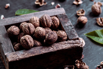 Box with tasty walnuts and nutcracker on dark wooden table, closeup