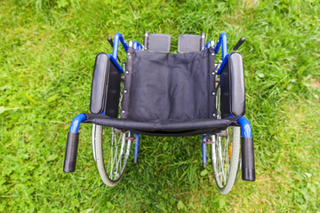 Empty wheelchair standing on grass in hospital park waiting for patient services. Invalid chair for...