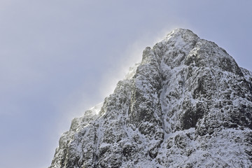Snow covered Buachaille Etive Mor mountain in Glencoe, Scottish Highlands. Zoomed in to show top only. Blue sky background.
