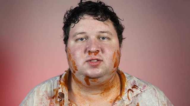 Man after meal. Fat and dirty man with tomato sauce spreading on his face in red background. Unhealthy concept