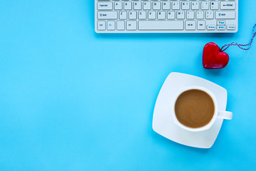 Keyboard, a cup of coffee and toy red heart on blue background. Valentines day concept. Top view, flat lay, copy space.