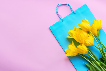 Yellow tulips and blue gift bag on a pink background. Women's Day concept. Top view, flat lay, copy space.