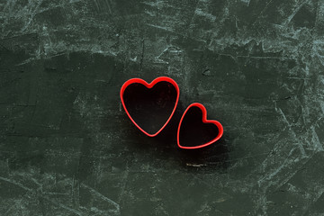 Creative holiday concept of love. Two cookie cutters in a shape of heart on a black chalk board. Top view, flat lay.