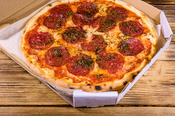 Pizza with salami sausage and parmesan cheese in cardboard box on a wooden table